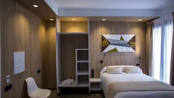 A modern hotel room with a bed, a built-in wardrobe, a seating area, and a wall-mounted artwork.