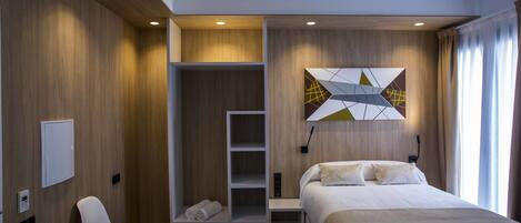 A modern hotel room with a bed, a built-in wardrobe, a seating area, and a wall-mounted artwork.