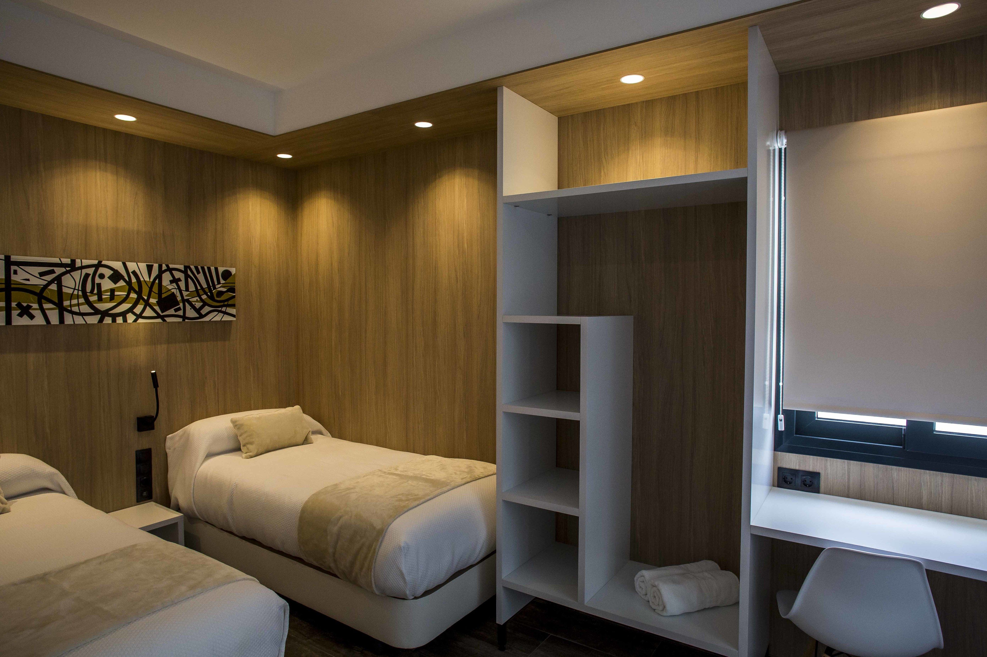 A modern hotel room with a wooden wall, a large bed, a desk, and a wardrobe.