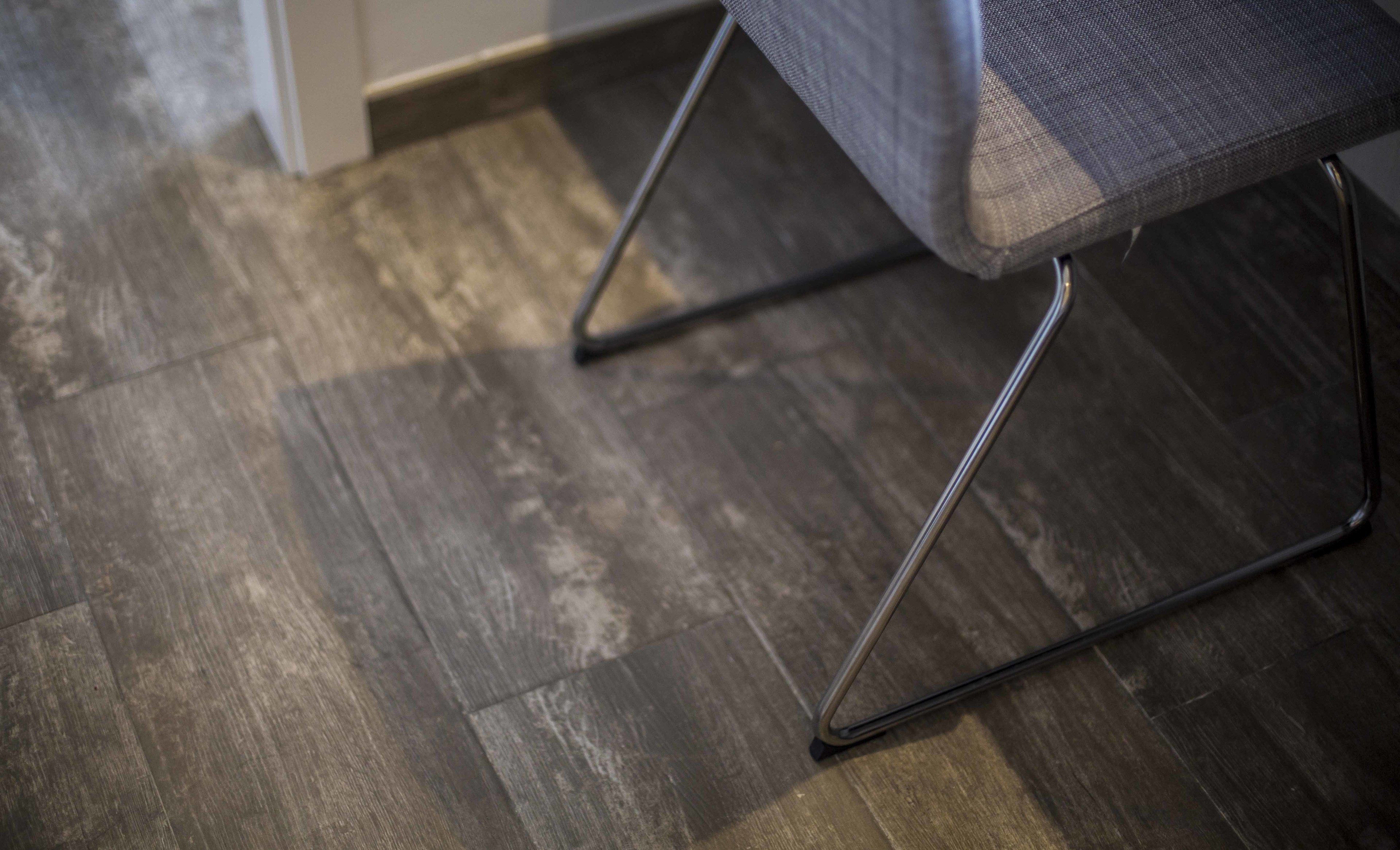 Gros plan d’une chaise aux pieds métalliques et à l’assise en tissu gris, placée sur un plancher en bois.