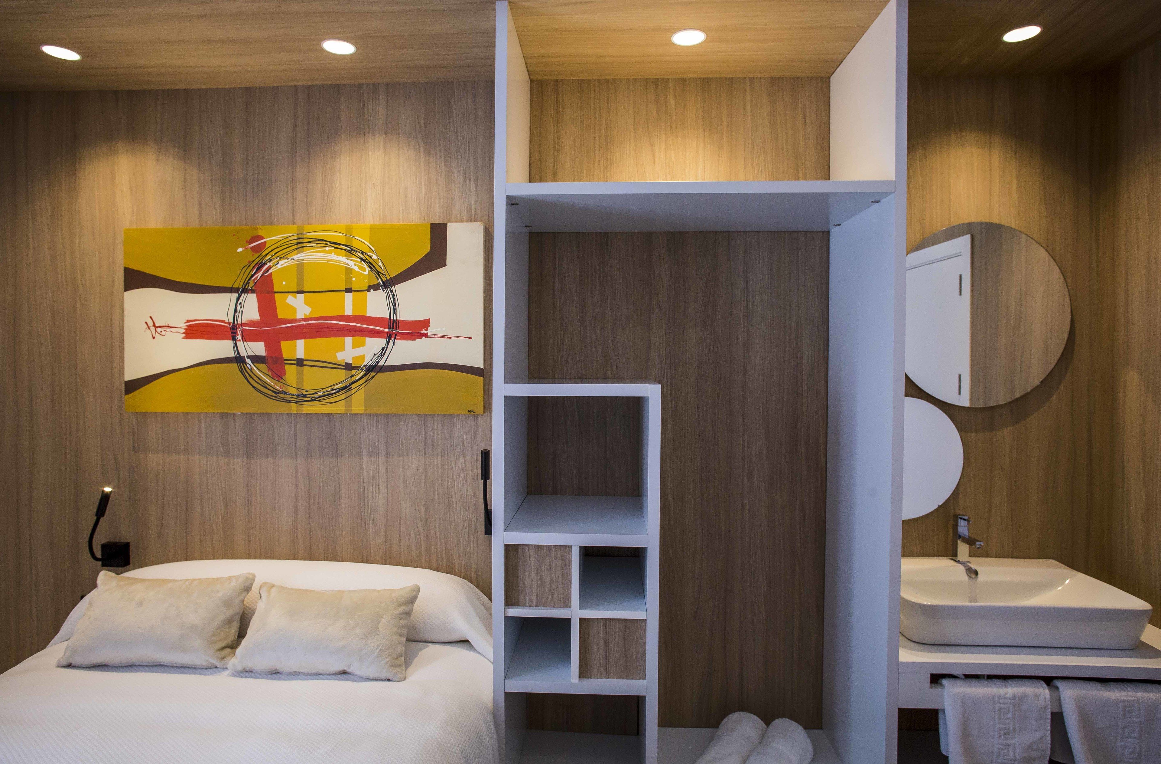 Un dormitorio moderno con cama, un armario blanco, un baño con lavabo y espejo, y una pared de madera.