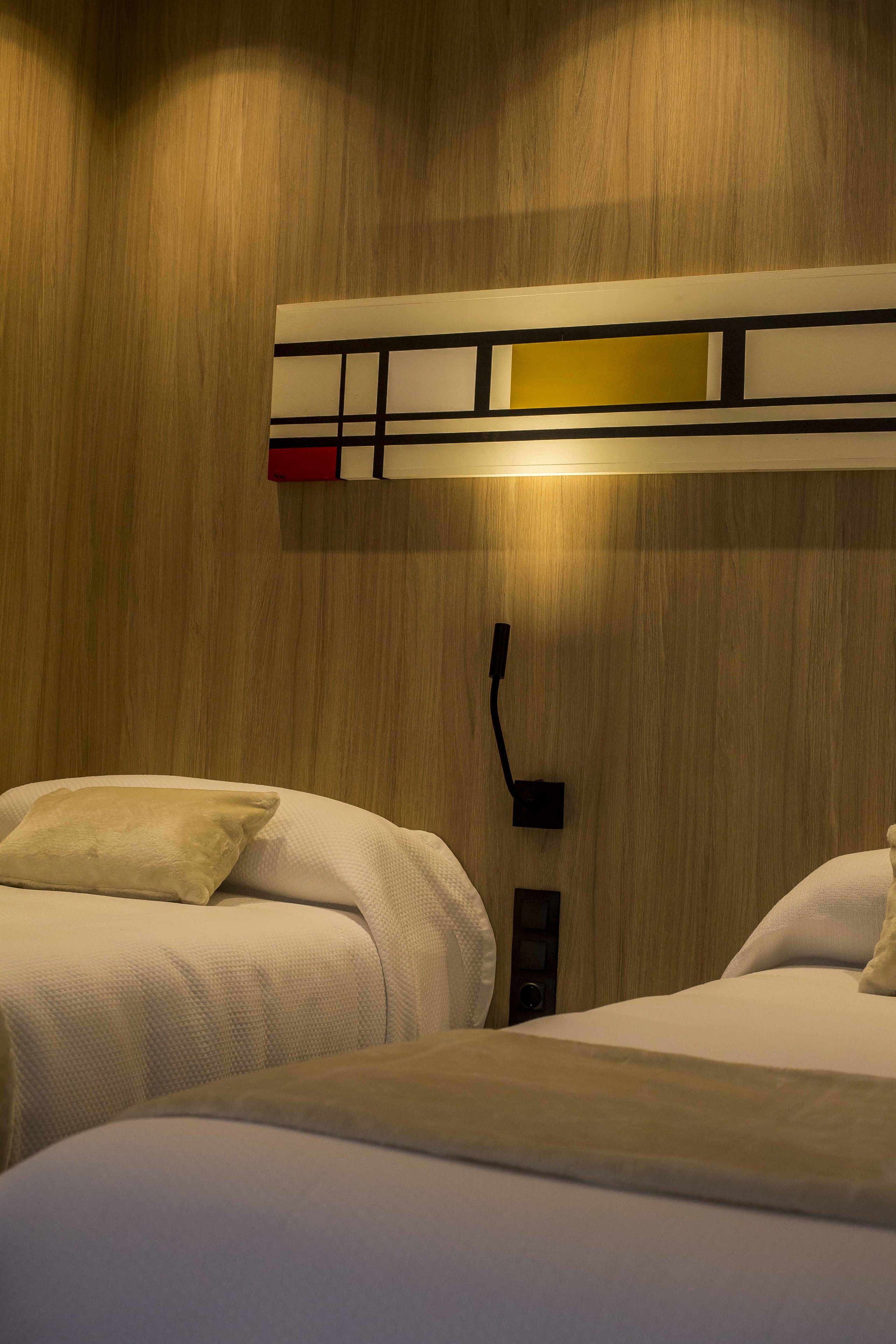 Quarto de hotel com duas camas, parede de madeira e luminária moderna.