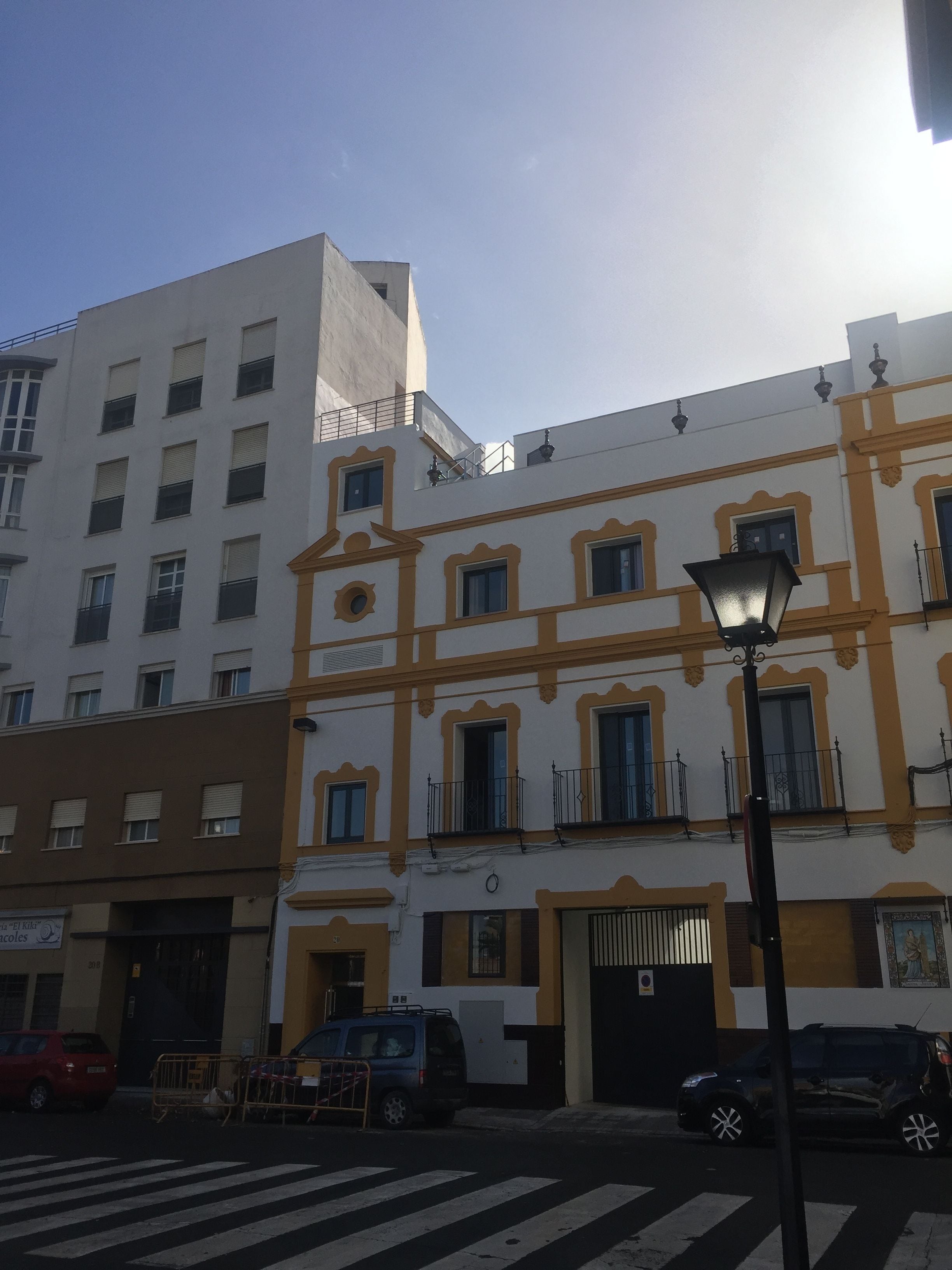 Une vue de rue avec un bâtiment dont la façade est blanche, agrémentée de bordures jaunes et de nombreuses fenêtres. Un lampadaire se trouve au premier plan.
