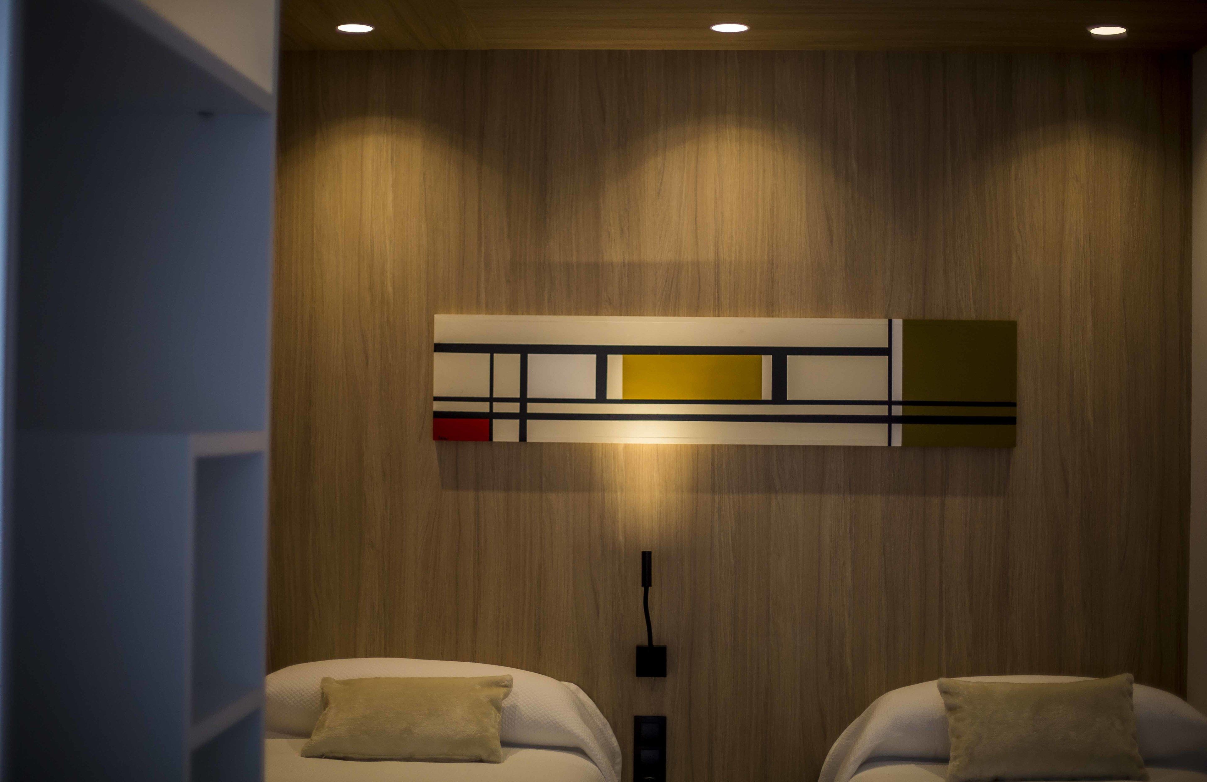 A hotel room with a wooden wall, a modern abstract artwork, and two beds with pillows.