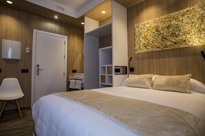 Habitación de hotel con una cama grande, una silla blanca, un baño con lavamanos y una obra de arte colgada en la pared.