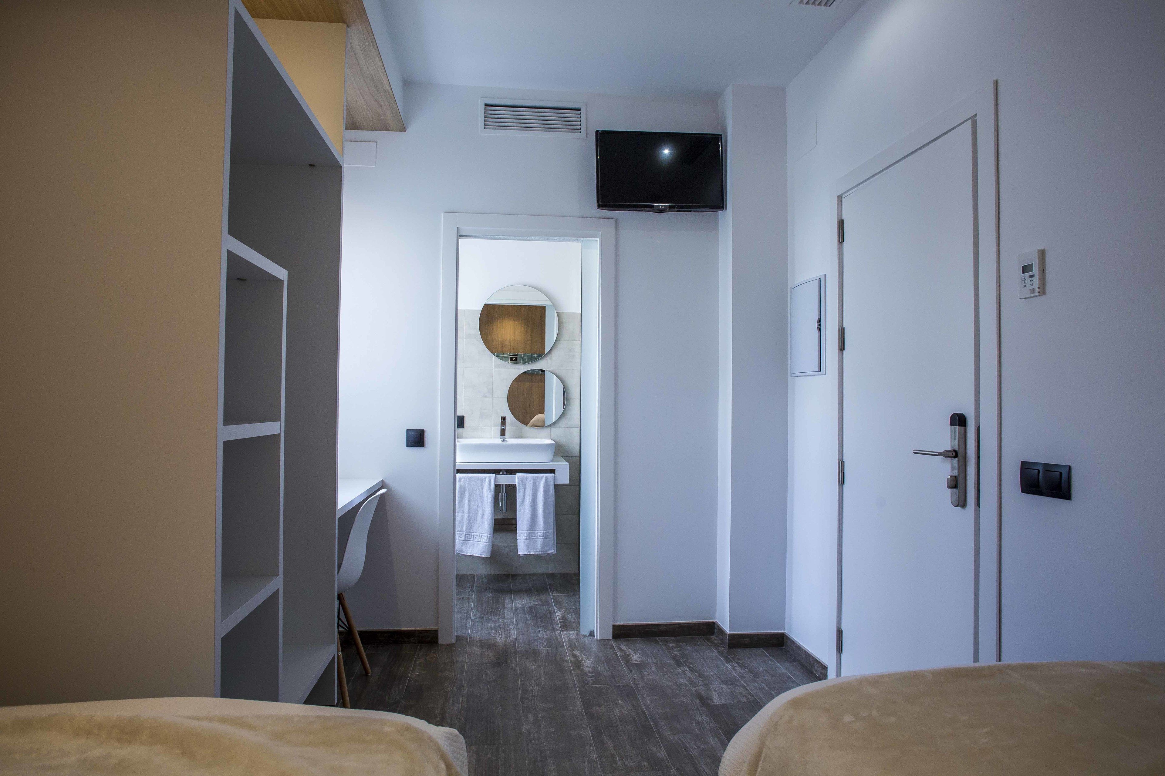 Habitación de hotel con cama, televisor montado en la pared, baño con lavabo y espejo, y armario.