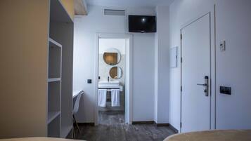 Une chambre d’hôtel comprenant un lit, un téléviseur fixé au mur, une salle de bain avec un lavabo et un miroir, et une armoire.
