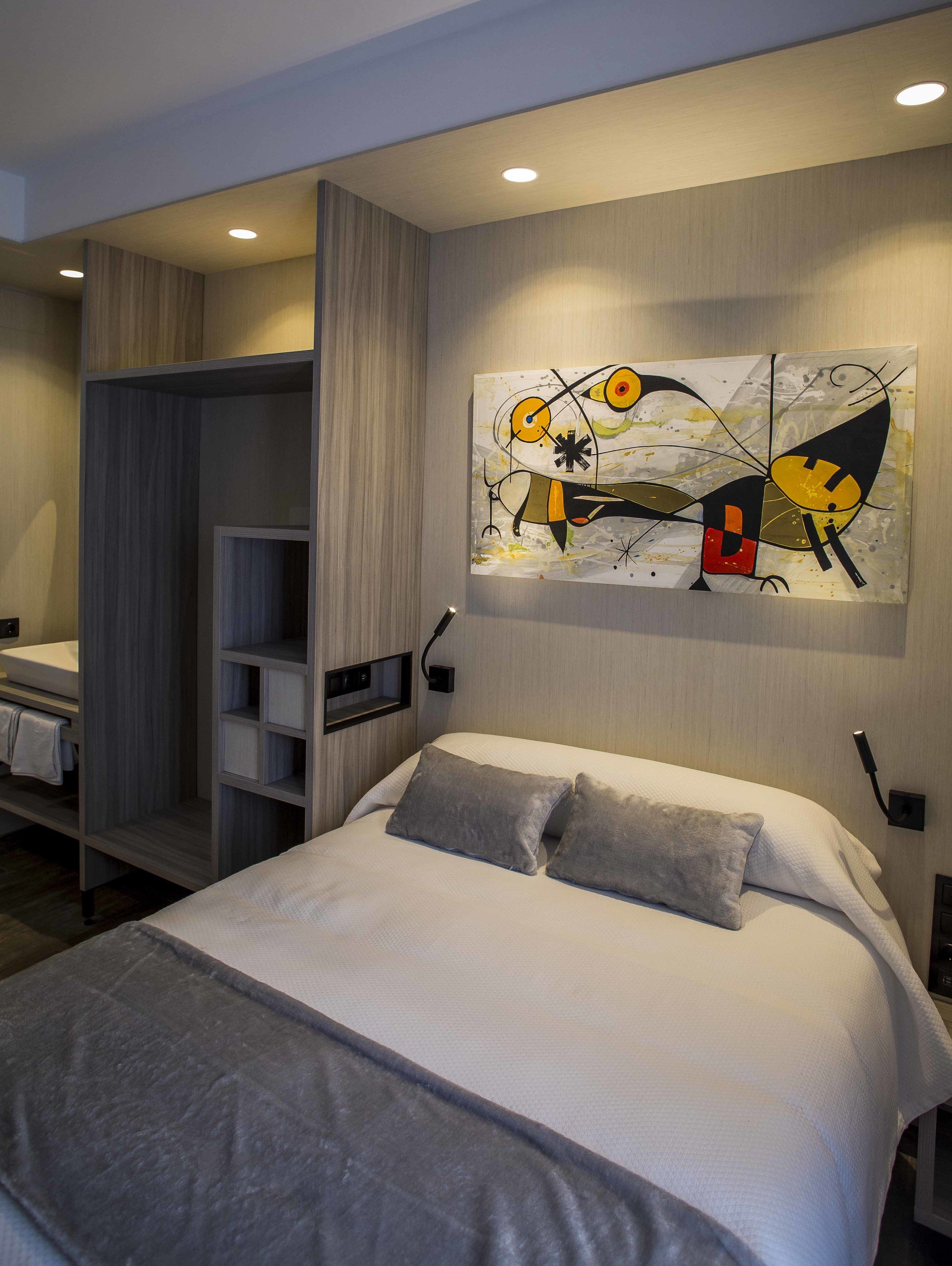 Una habitación de hotel moderna con una cama, un armario y un cuadro abstracto colgado en la pared.