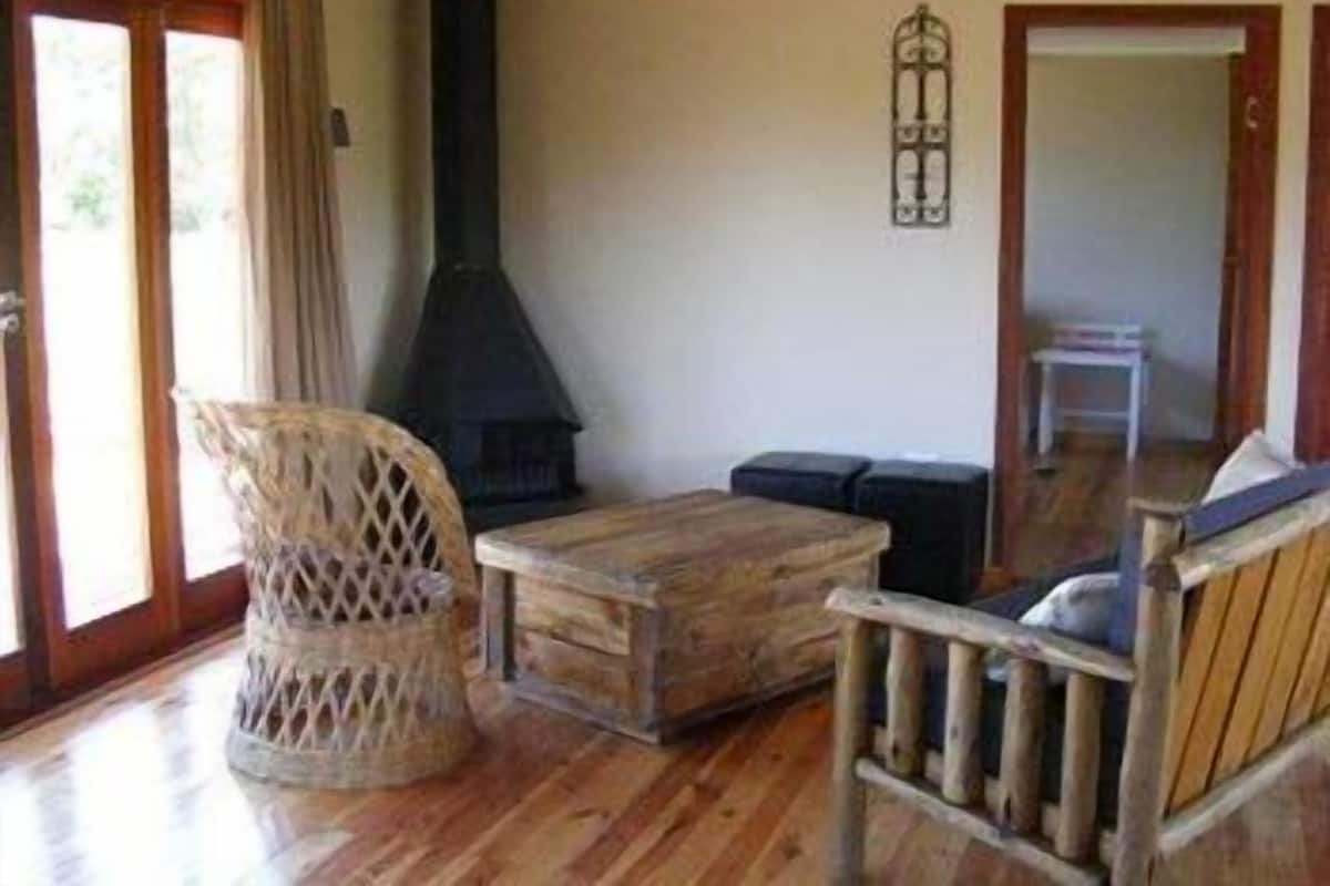 Een gezellige kamer met houten vloer, een rieten stoel, een houten tafel en een zwart haardvuur.