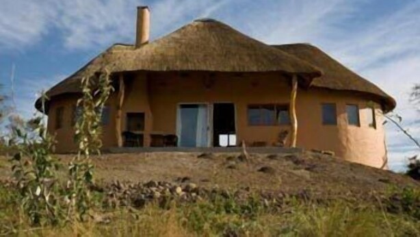 Ein Haus mit einem Reetdach, einem flachen Dach, einem Schornstein und einer Tür, die zu einem Innenraum führt.