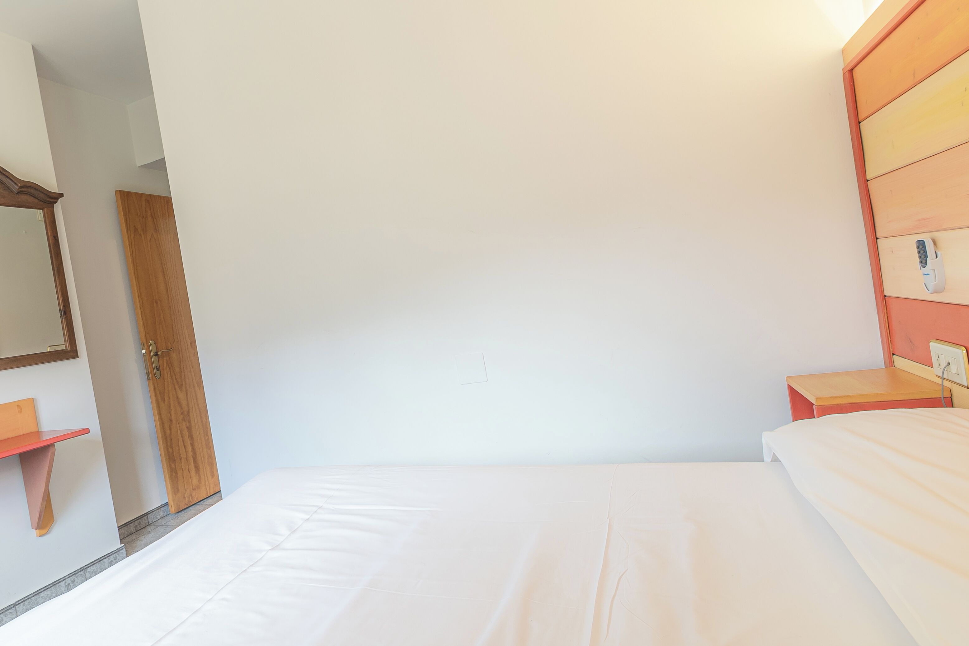 Un dormitorio con una cama individual, un armario de madera, una mesita de noche pequeña y una mesita de noche con una lámpara.
