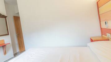 A bedroom with a single bed, a wooden wardrobe, a small bedside table, and a nightstand with a lamp.