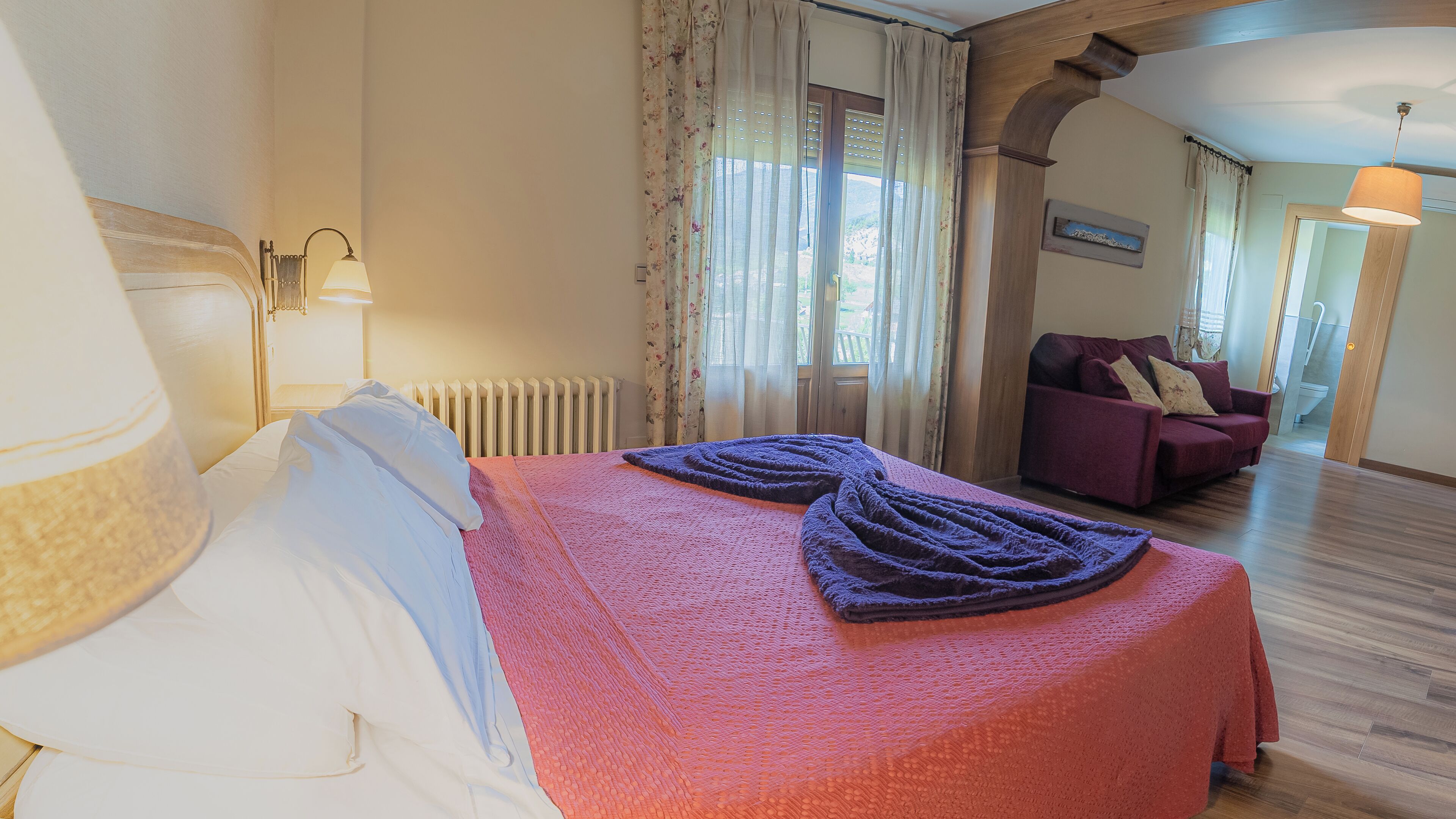 Una habitación de hotel con una cama, un sofá, un radiador y una ventana con cortinas.