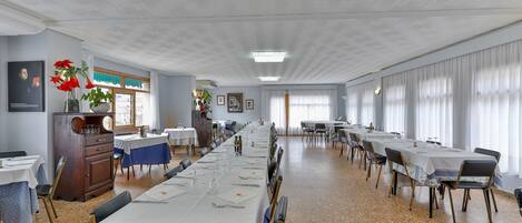 Un comedor amplio con mesas dispuestas para una comida, un armario de madera y una ventana con cortinas.