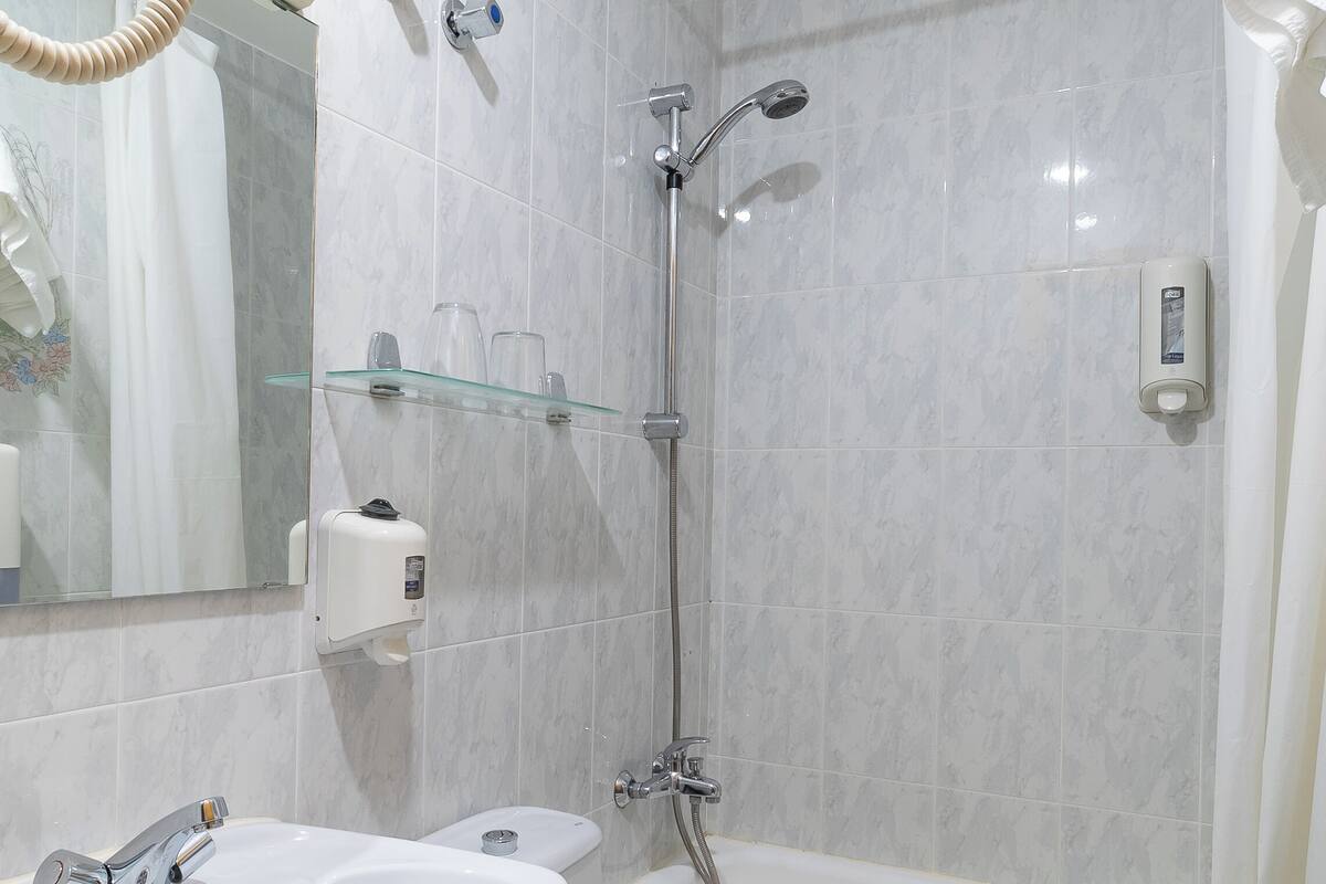 A bathroom with a white sink, toilet, and bathtub. There is a glass shelf above the sink with toiletries.
