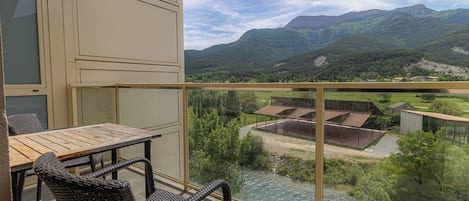 A balcony with wicker furniture overlooking a river and mountains.
