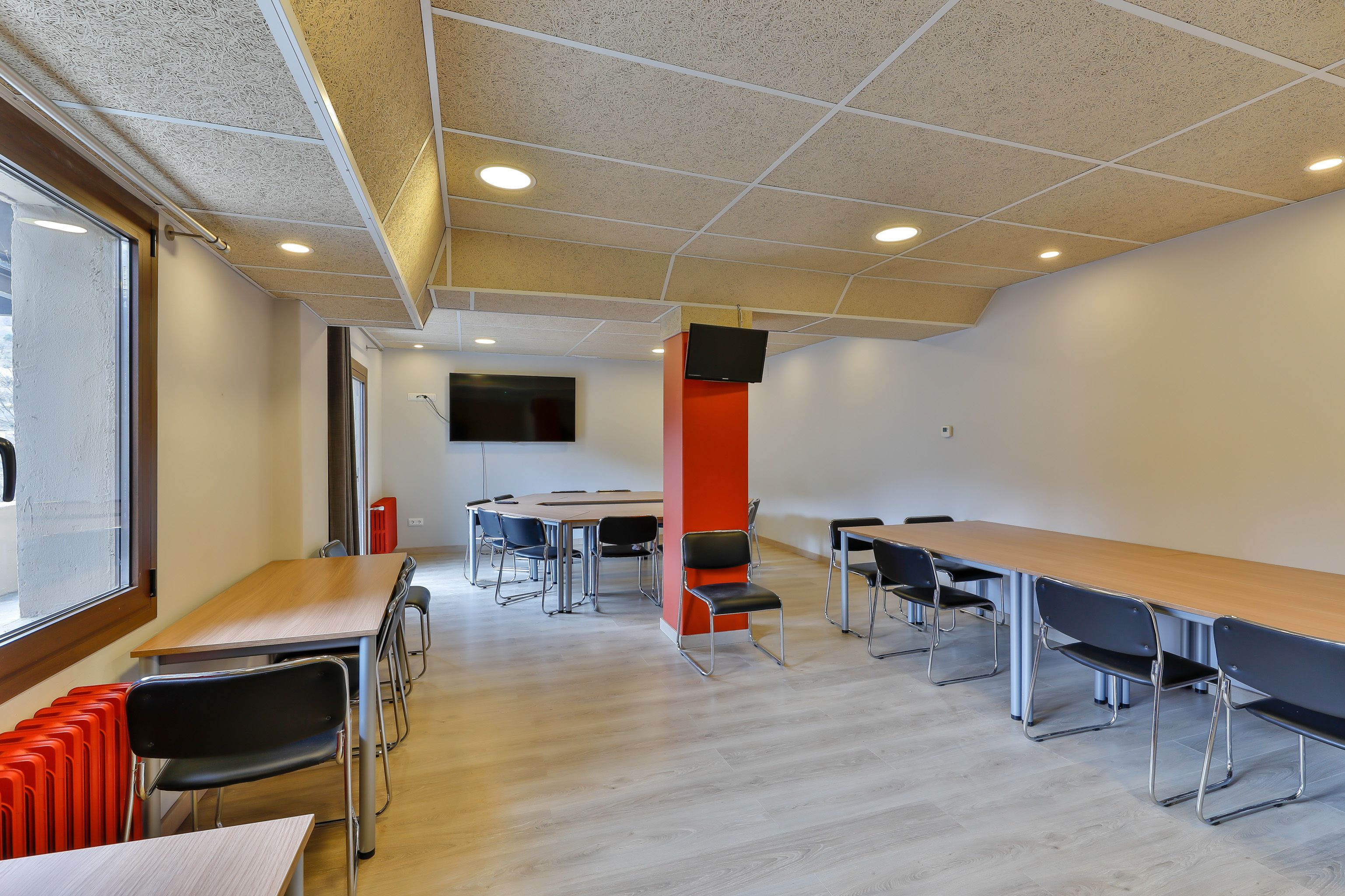Un salón de conferencias con una larga mesa, múltiples sillas, una pared de acento roja y un televisor de pantalla plana montado en la pared.