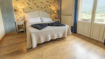 A bedroom with a bed, two bedside tables, a lamp, a window with a view, and a patterned wallpaper.