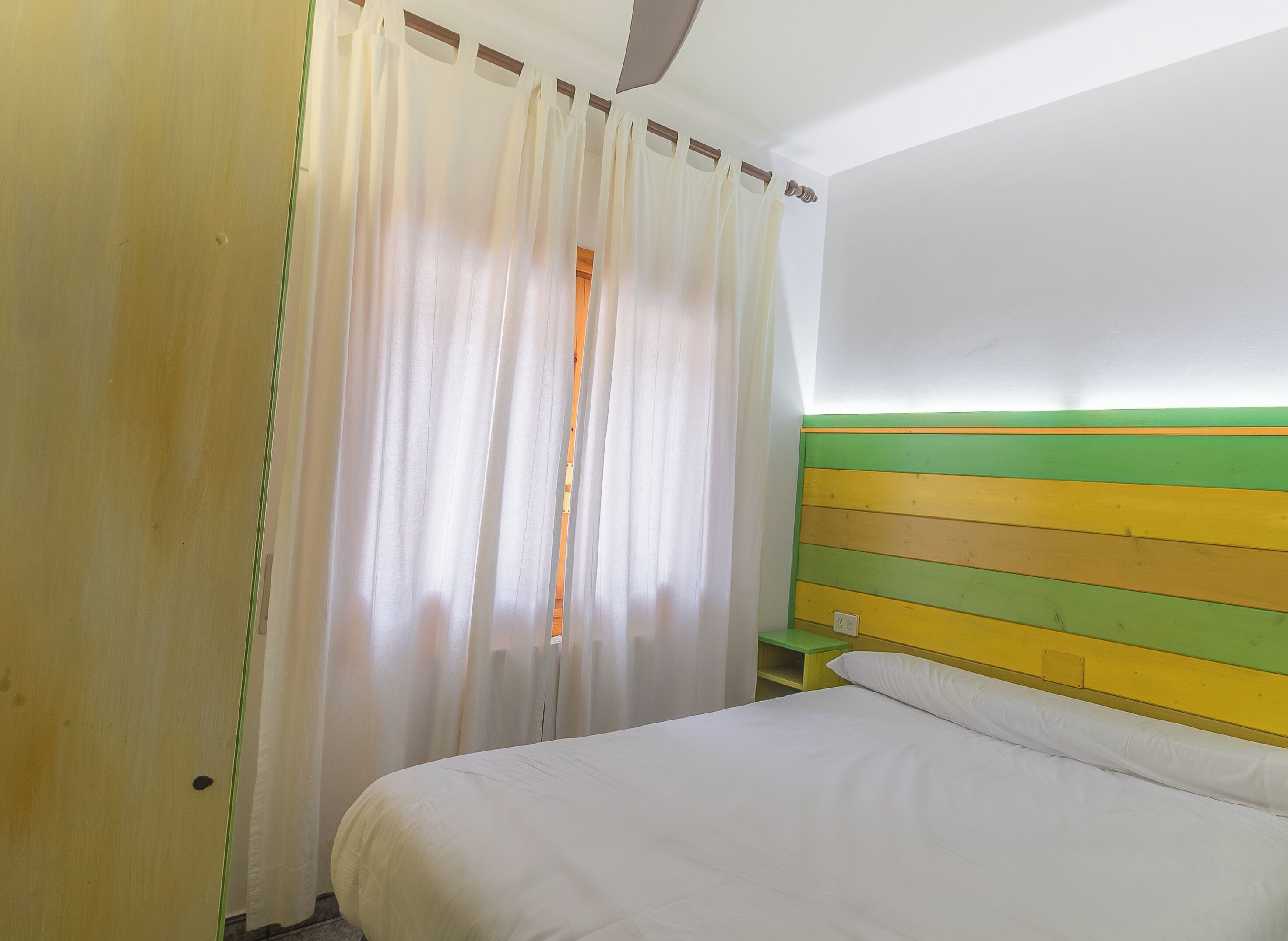 Una habitación con cama, mesita de noche y ventana con cortinas.