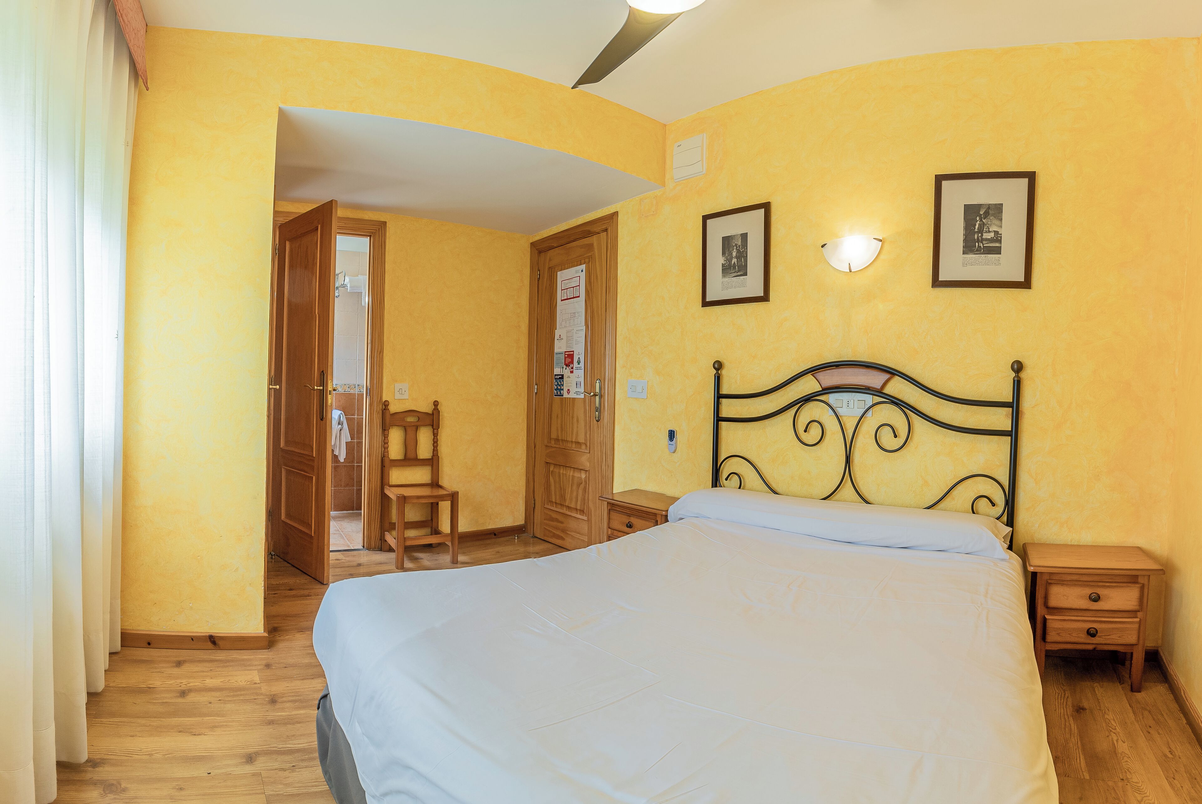 Une chambre à coucher avec un lit, une table de chevet en bois et une porte donnant sur une autre pièce.