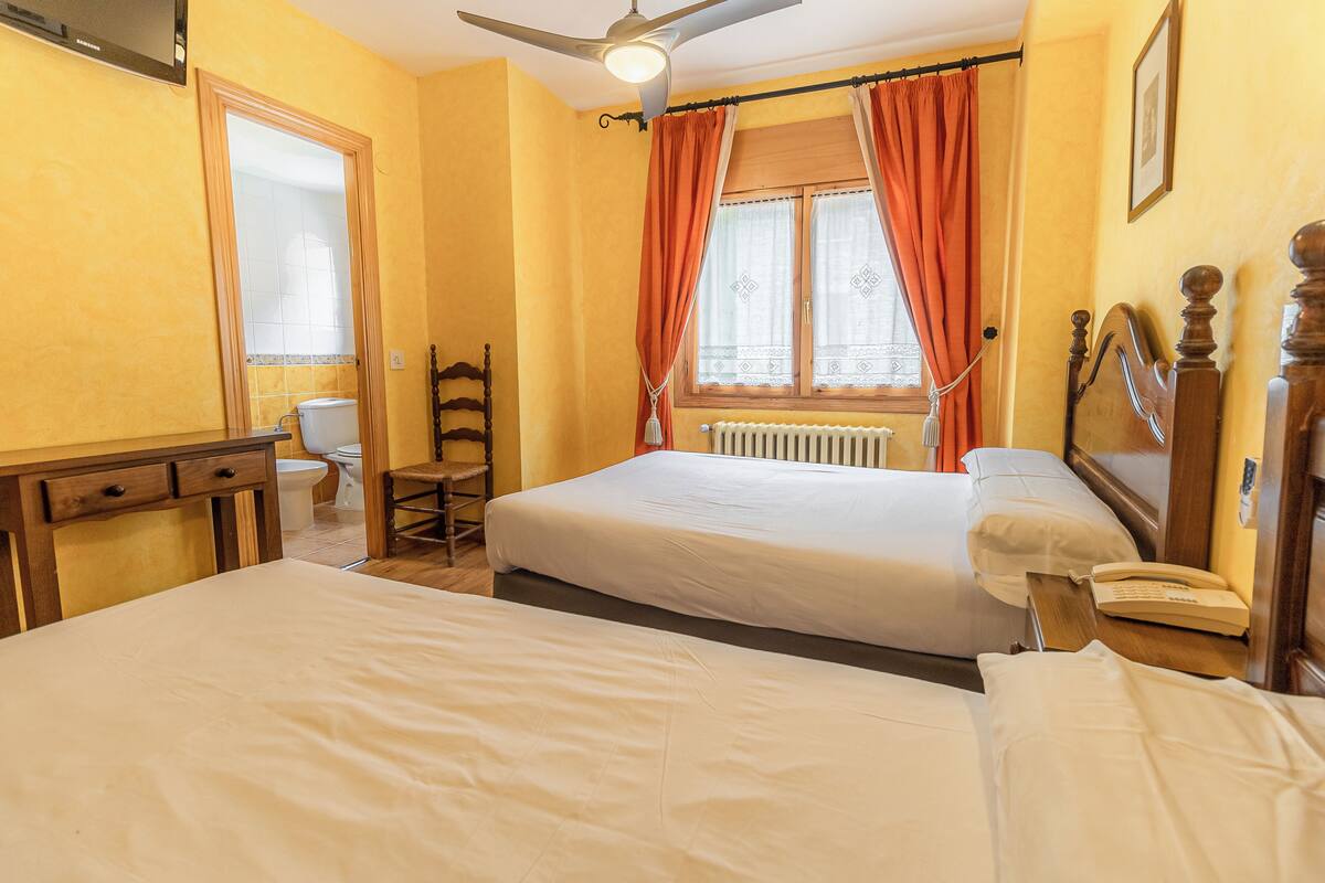 A hotel room with two beds, a desk, a chair, a toilet, and a window with curtains.