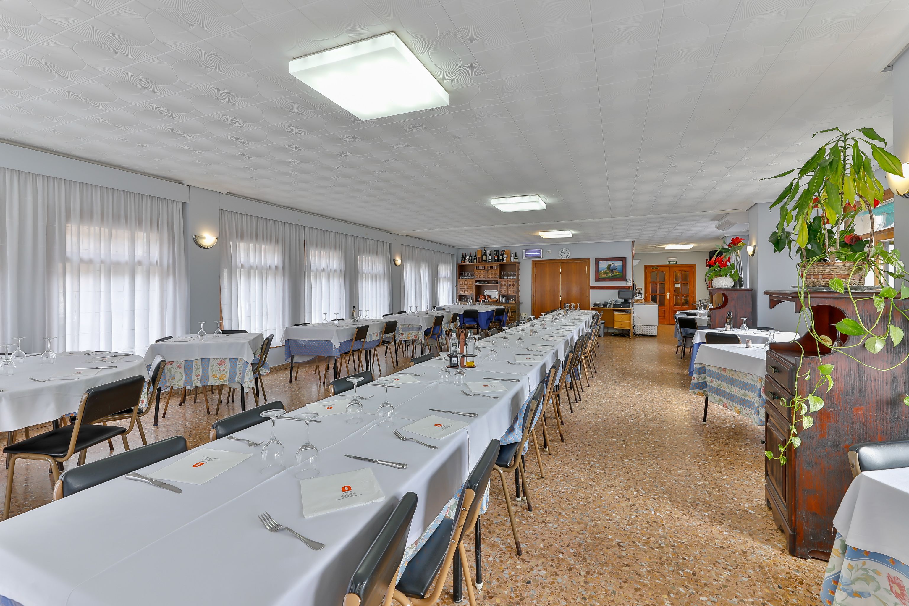 A long dining table set with white tablecloths, chairs, and dining utensils.