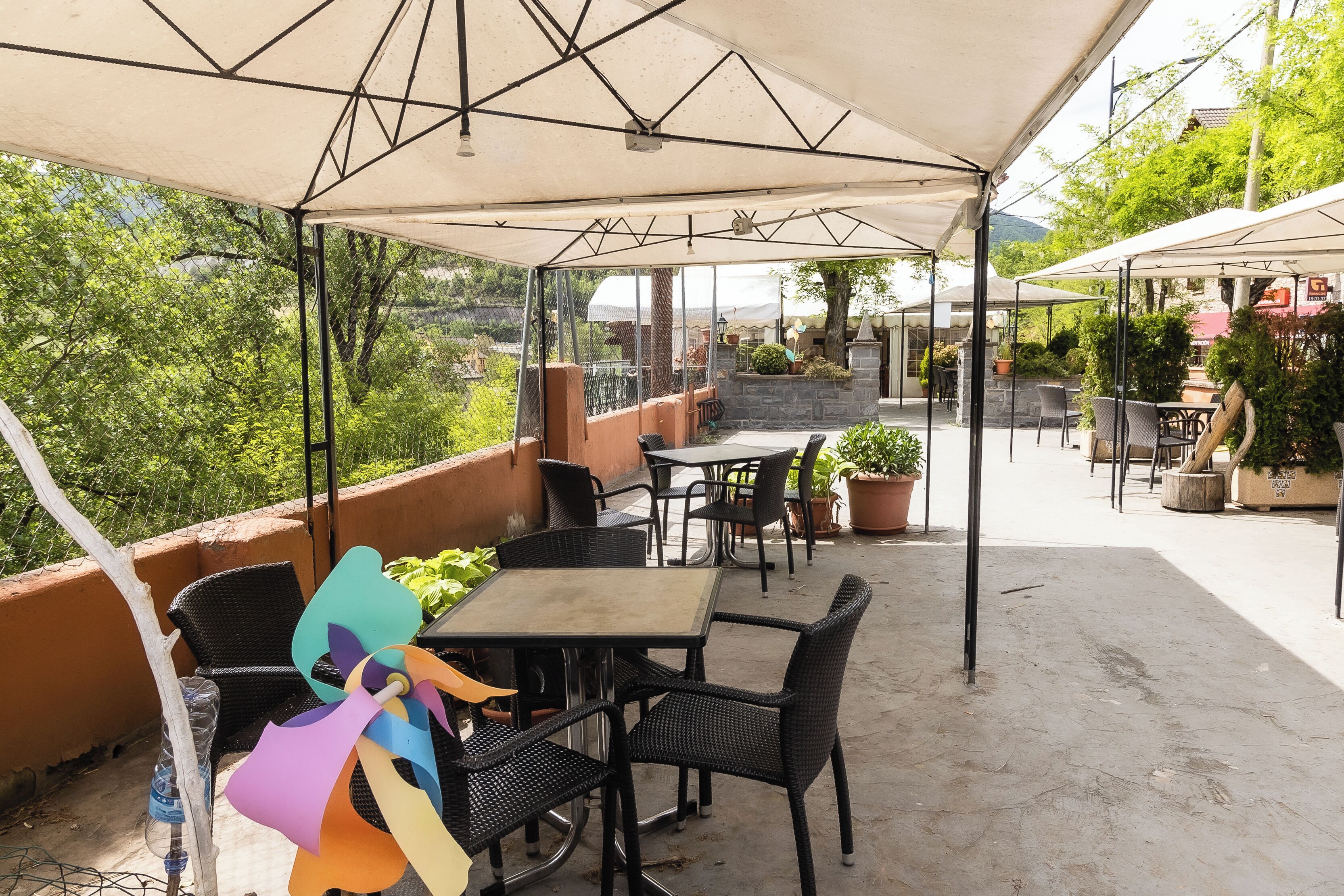 An outdoor patio with tables and chairs, surrounded by potted plants and a view of greenery.