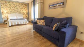 Una habitación con cama, sofá azul, suelo de madera y papel tapiz estampado.