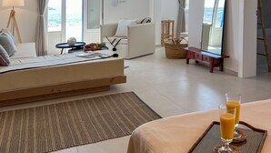 Une chambre d’hôtel moderne avec un lit, un canapé, une table à manger avec des boissons, et une vue sur la mer.
