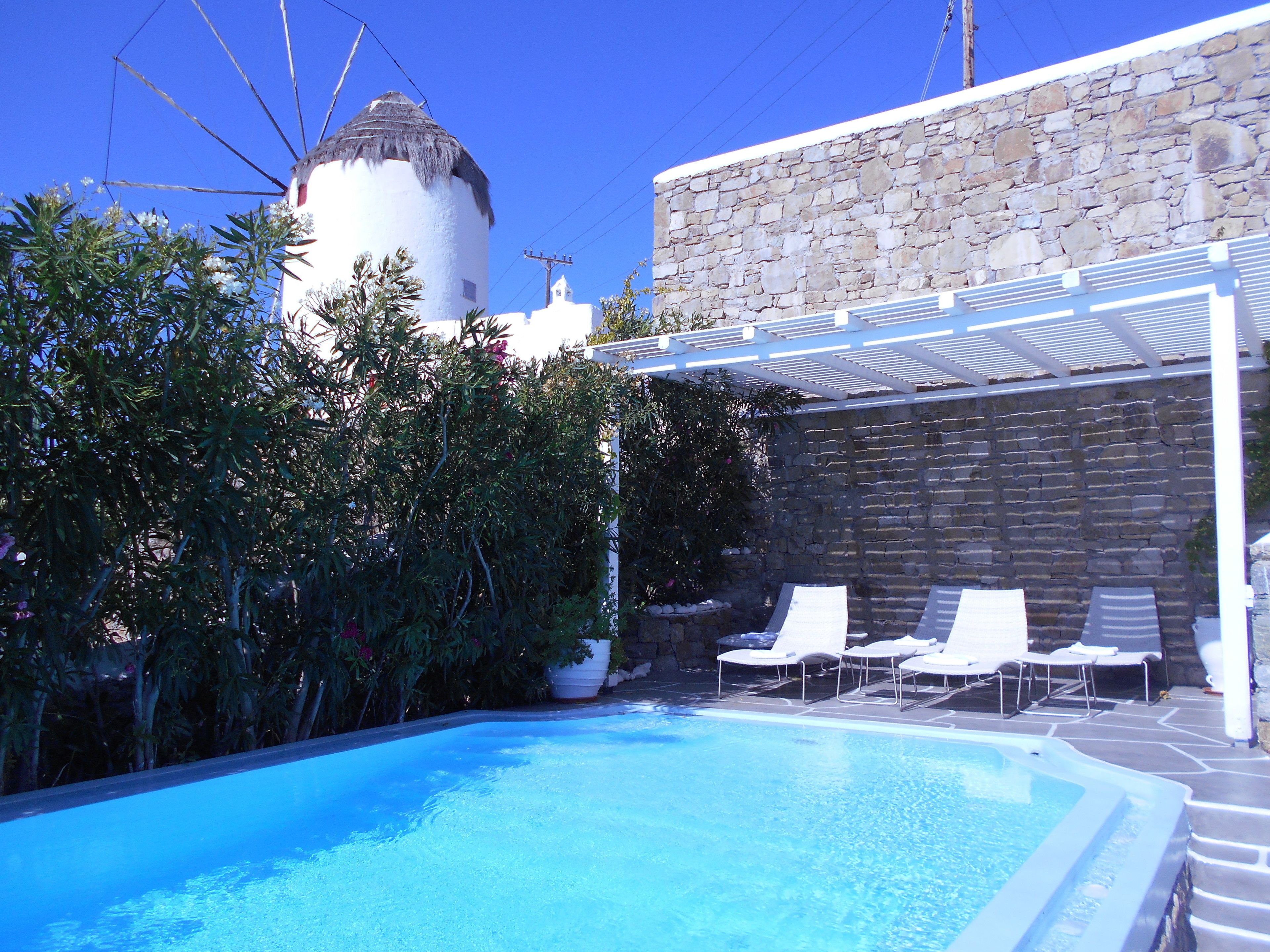 A swimming pool with lounge chairs, a stone wall, and a white building with a thatched roof.