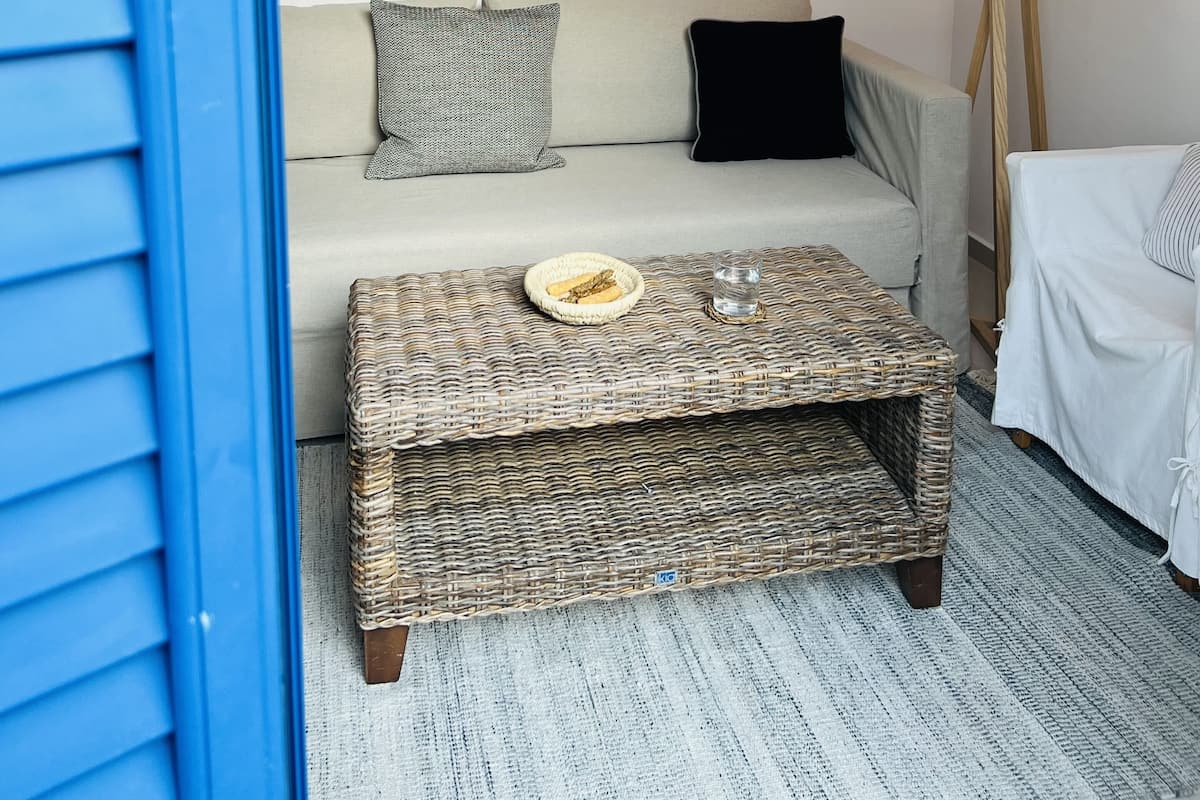 Un salon chaleureux avec un canapé de couleur claire, une table basse en osier et une lampe sur pied. Deux œuvres d’art sont accrochées au mur au-dessus du canapé.