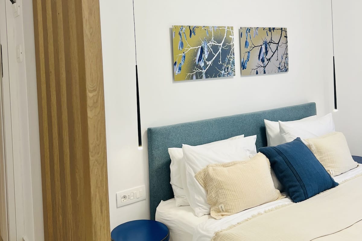 Une chambre moderne avec un lit, un tabouret bleu et deux œuvres d’art accrochées au mur.