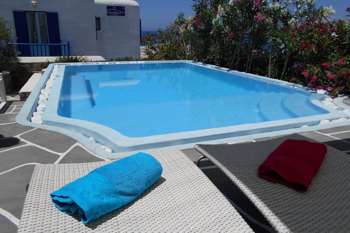 Une piscine dont le bord est revêtu de carreaux blancs et bleus, entourée d’une terrasse en pierre.