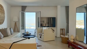 Une chambre d’hôtel avec un lit, un canapé, une télévision et vue sur la mer.
