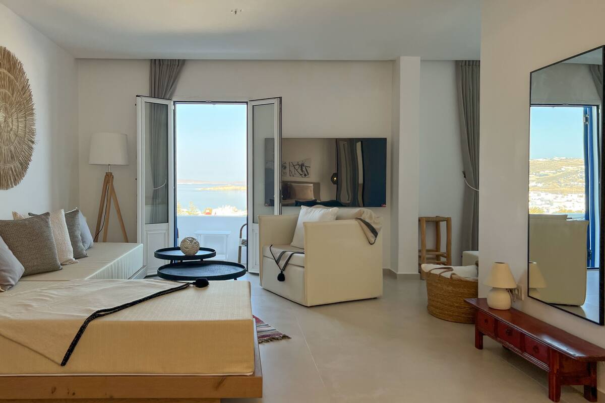 Une chambre d’hôtel avec un lit, un canapé, une télévision et vue sur la mer.