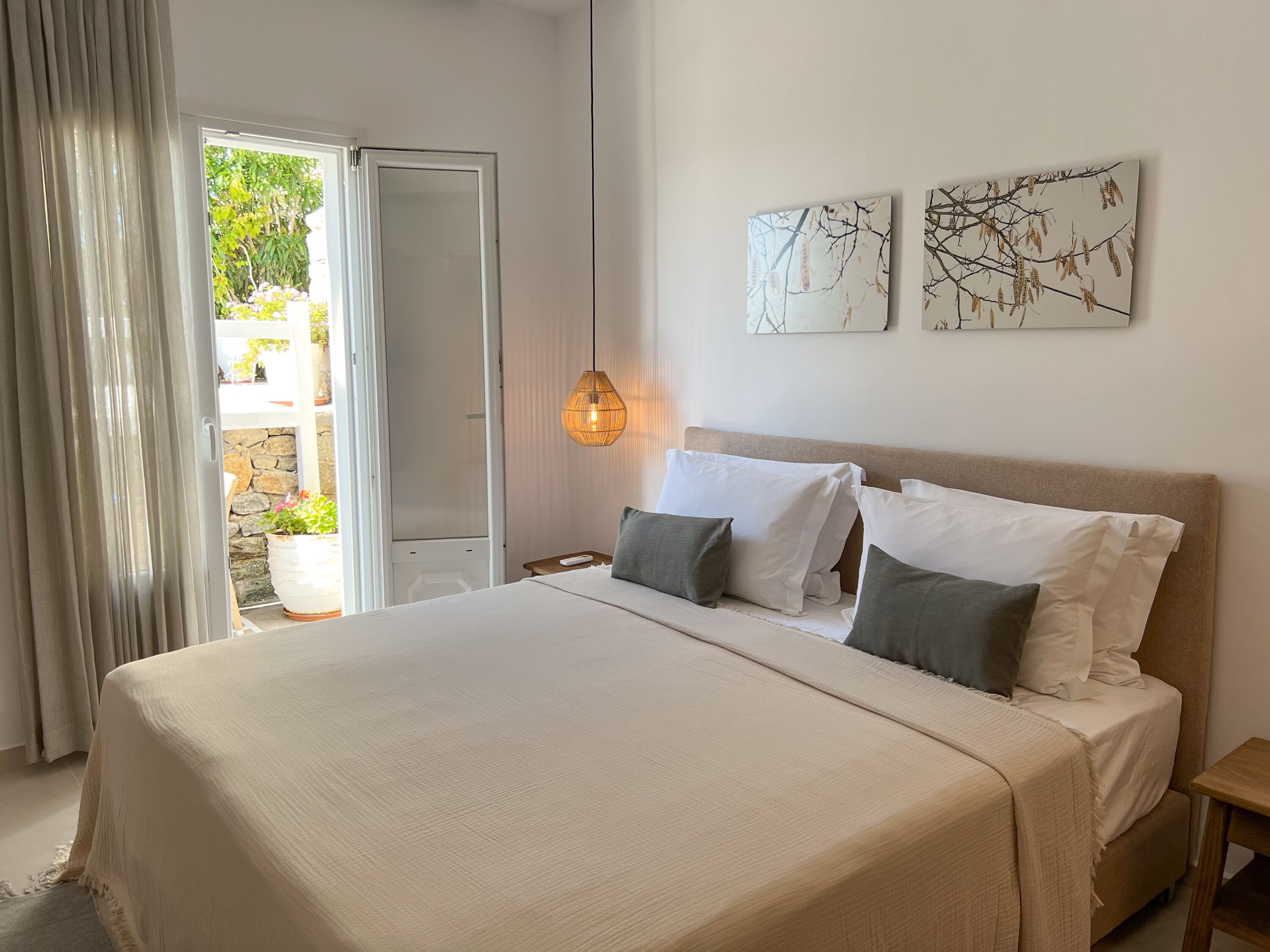 A bedroom with a large bed, a wooden nightstand, a hanging light, and two wall-mounted artworks.