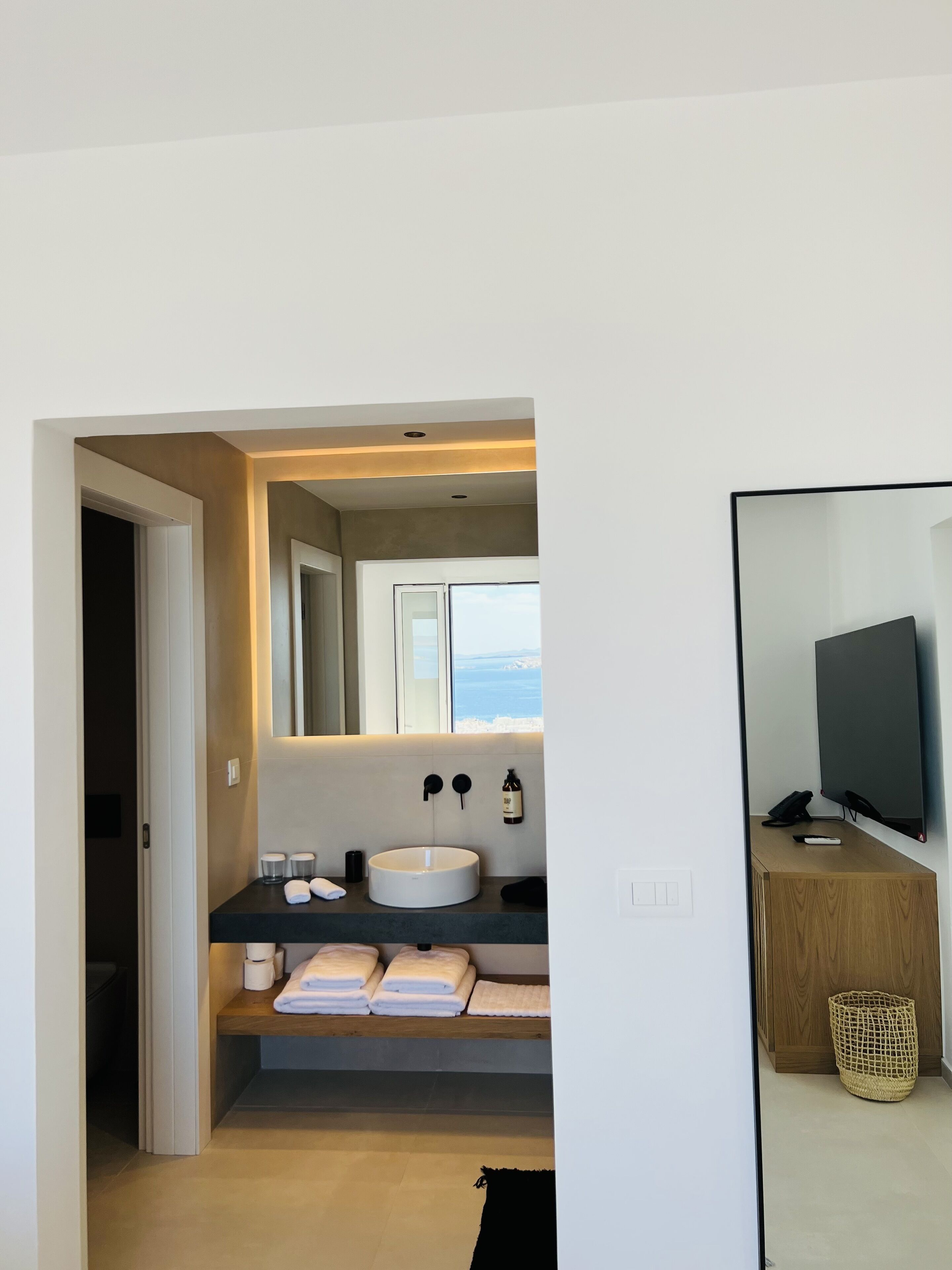A modern bathroom with a large sink, mirror, and a view of the sea.
