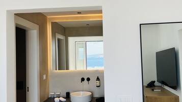 A modern bathroom with a large sink, mirror, and a view of the sea.