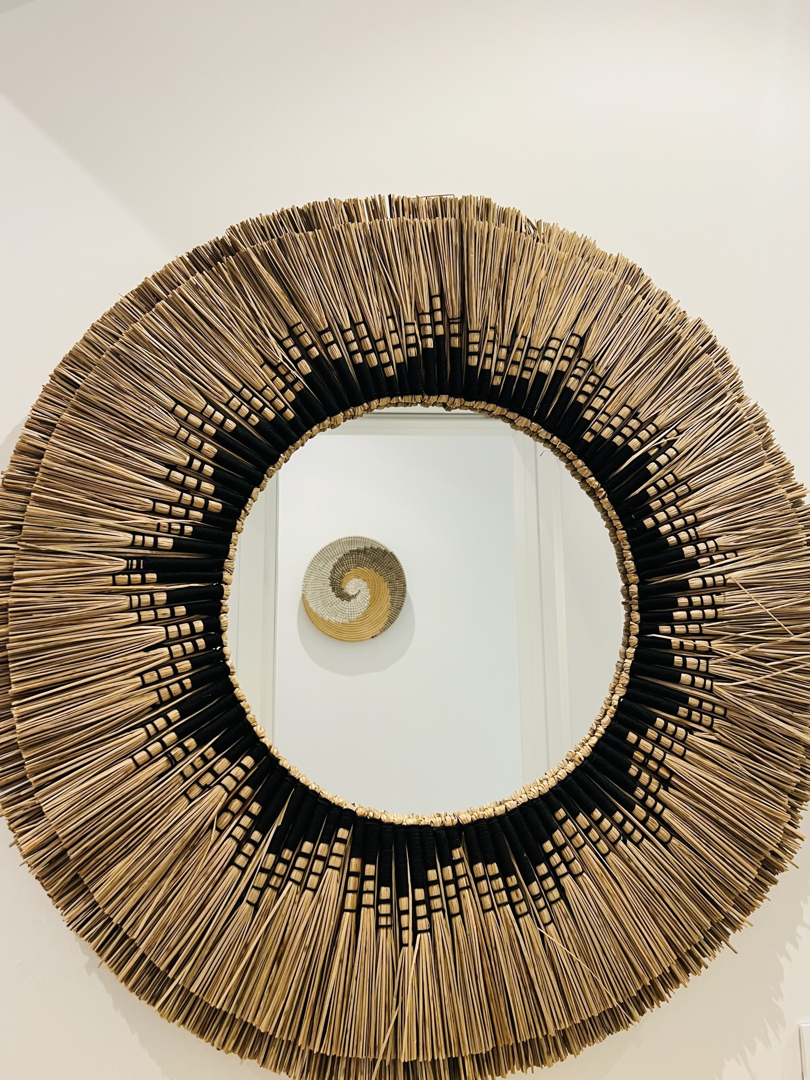 A circular wall mirror with a black and gold frame, surrounded by a spiral design.