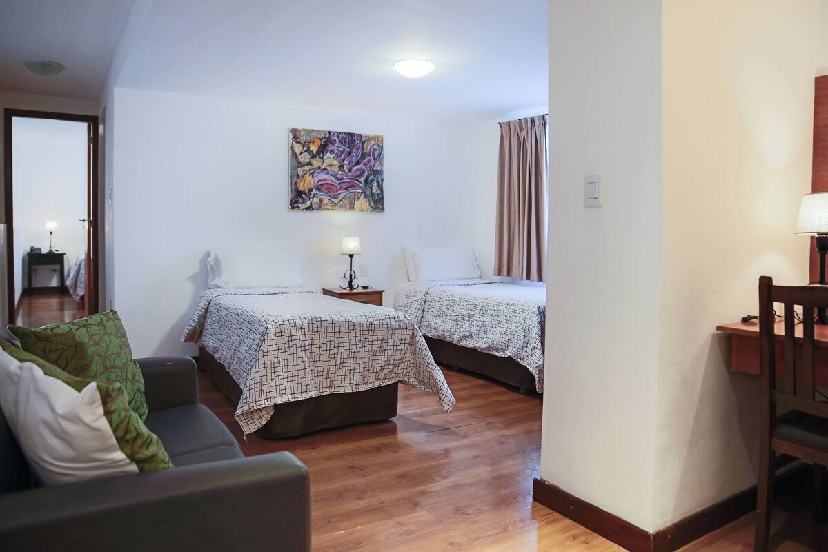 Ein Zimmer mit zwei Betten, einem Schlafsofa, einem Schreibtisch und einem Bild an der Wand.
