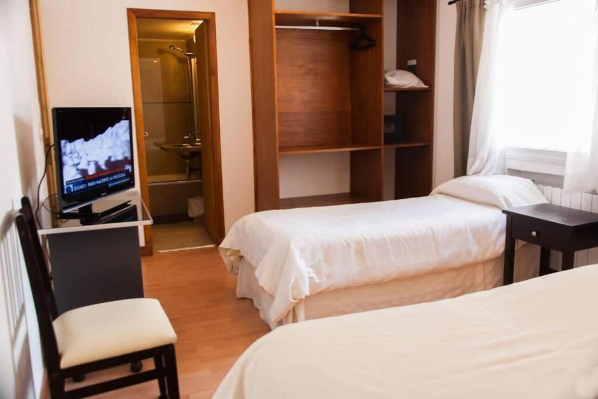 Ein Hotelzimmer mit zwei Betten, einem Fernseher, einem Schreibtisch und einem begehbaren Kleiderschrank.