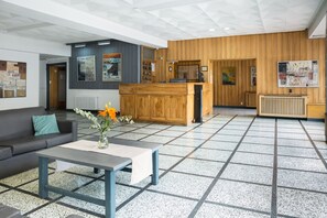 Een hal met een receptiebalie, een bank, een bijzettafeltje en een betegelde vloer.
