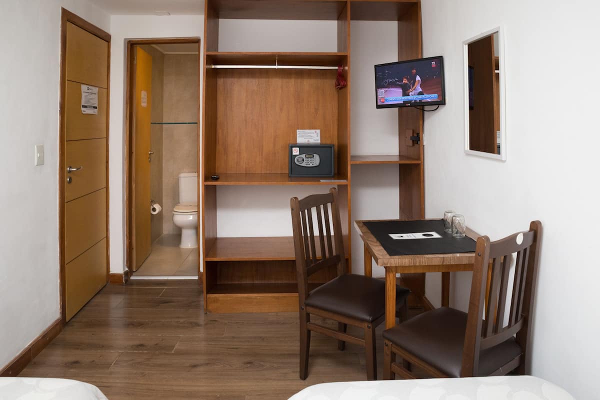 Ein Hotelzimmer mit Holzschrank, kleinem Tisch mit Stühlen, Fernseher und begehbarer Toilette.