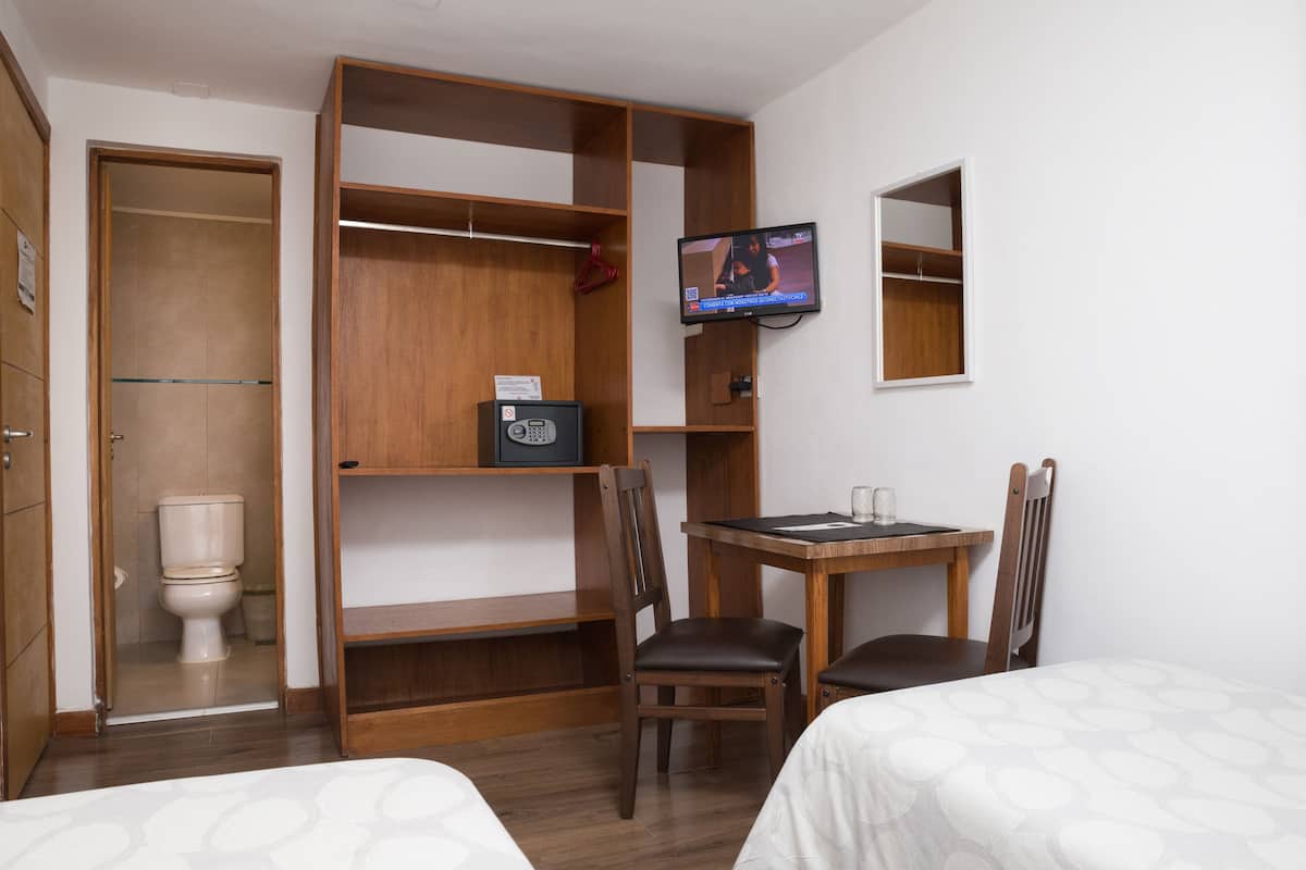 Ein Hotelzimmer mit einem Holzschrank, einem Schreibtisch mit Stuhl, einem Fernseher und zwei Betten.