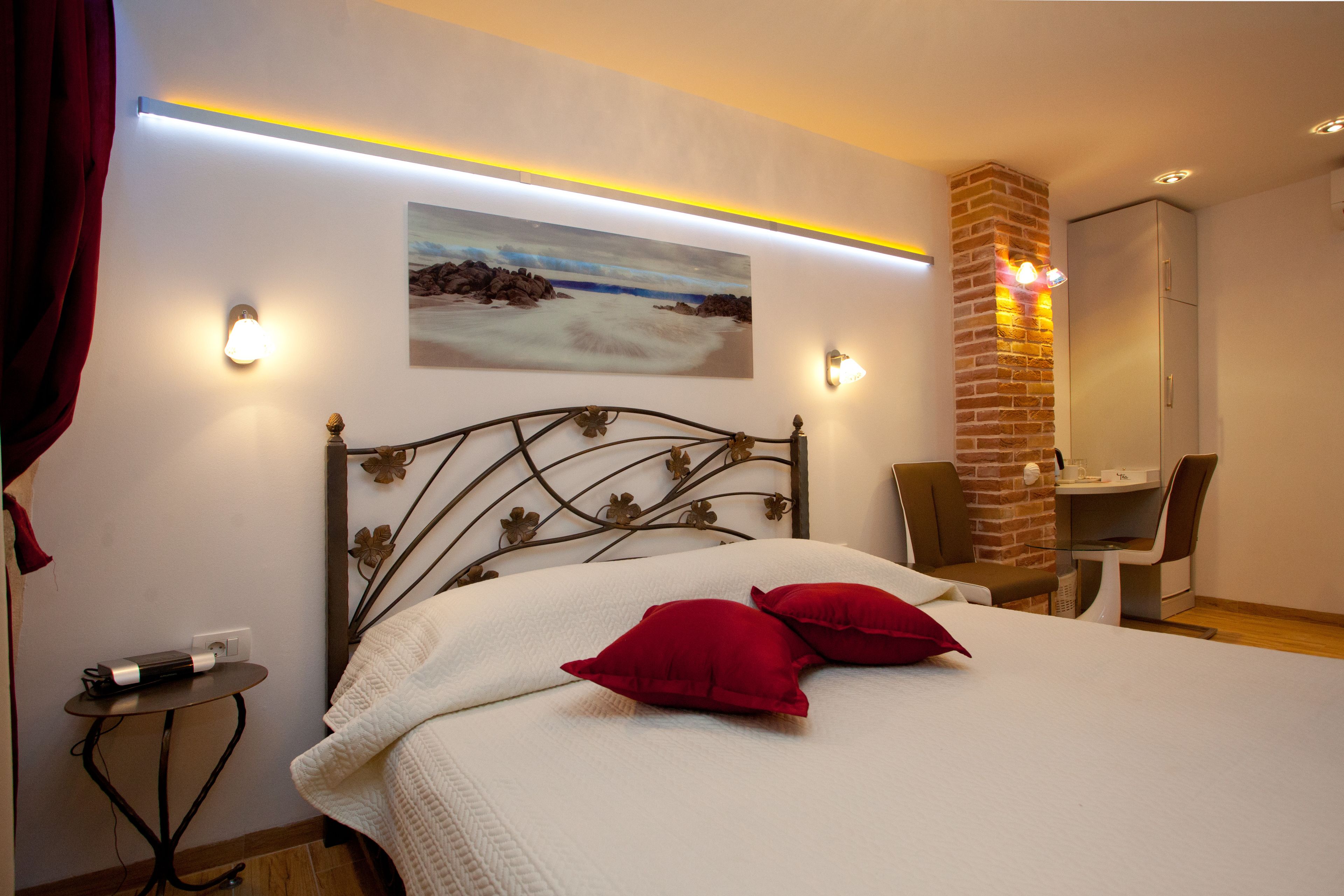 Ein Schlafzimmer mit einem Bett, roten Kissen, einem Bild an der Wand, einem Schreibtisch und einem Stuhl.