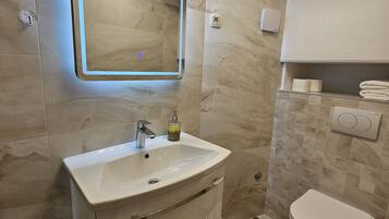 A modern bathroom with a white vanity, a mirror with under-cabinet lighting, a toilet, and a towel rack.