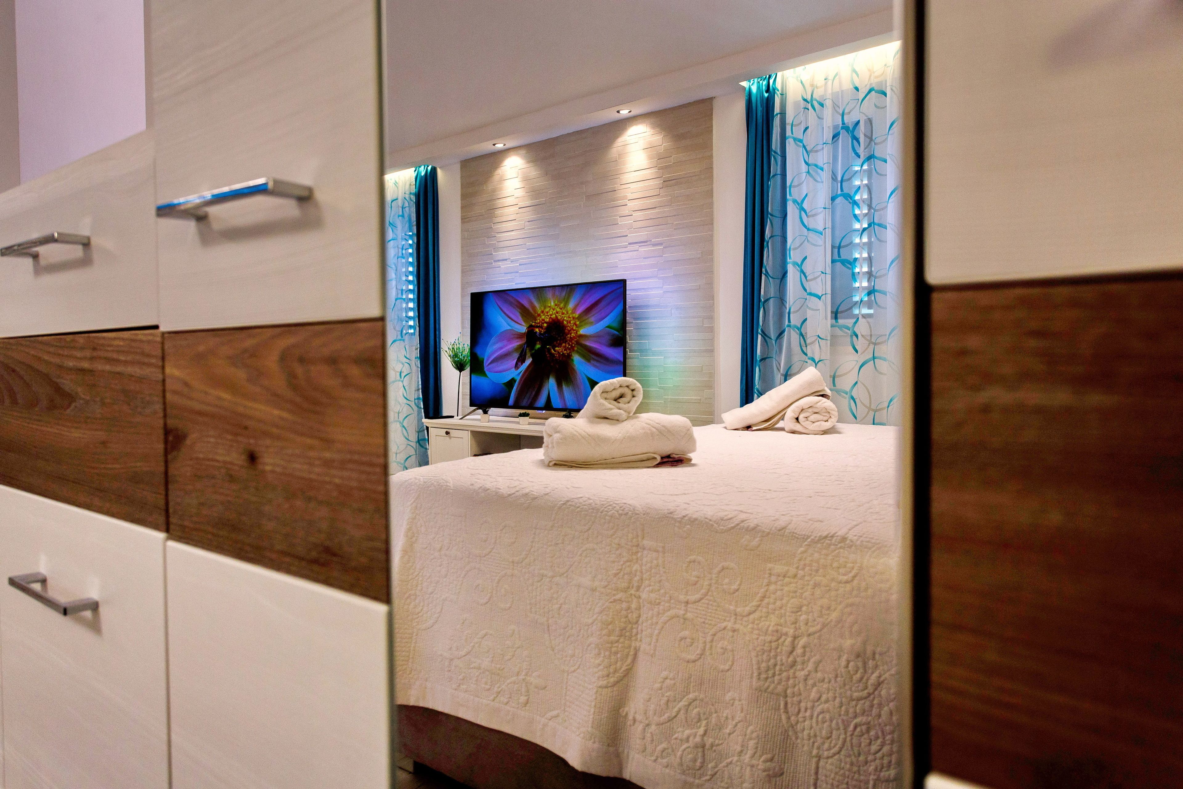 Une chambre d’hôtel moderne dotée d’un grand lit, d’un téléviseur à écran plat fixé au mur et d’une salle de bain avec un meuble-lavabo en bois.