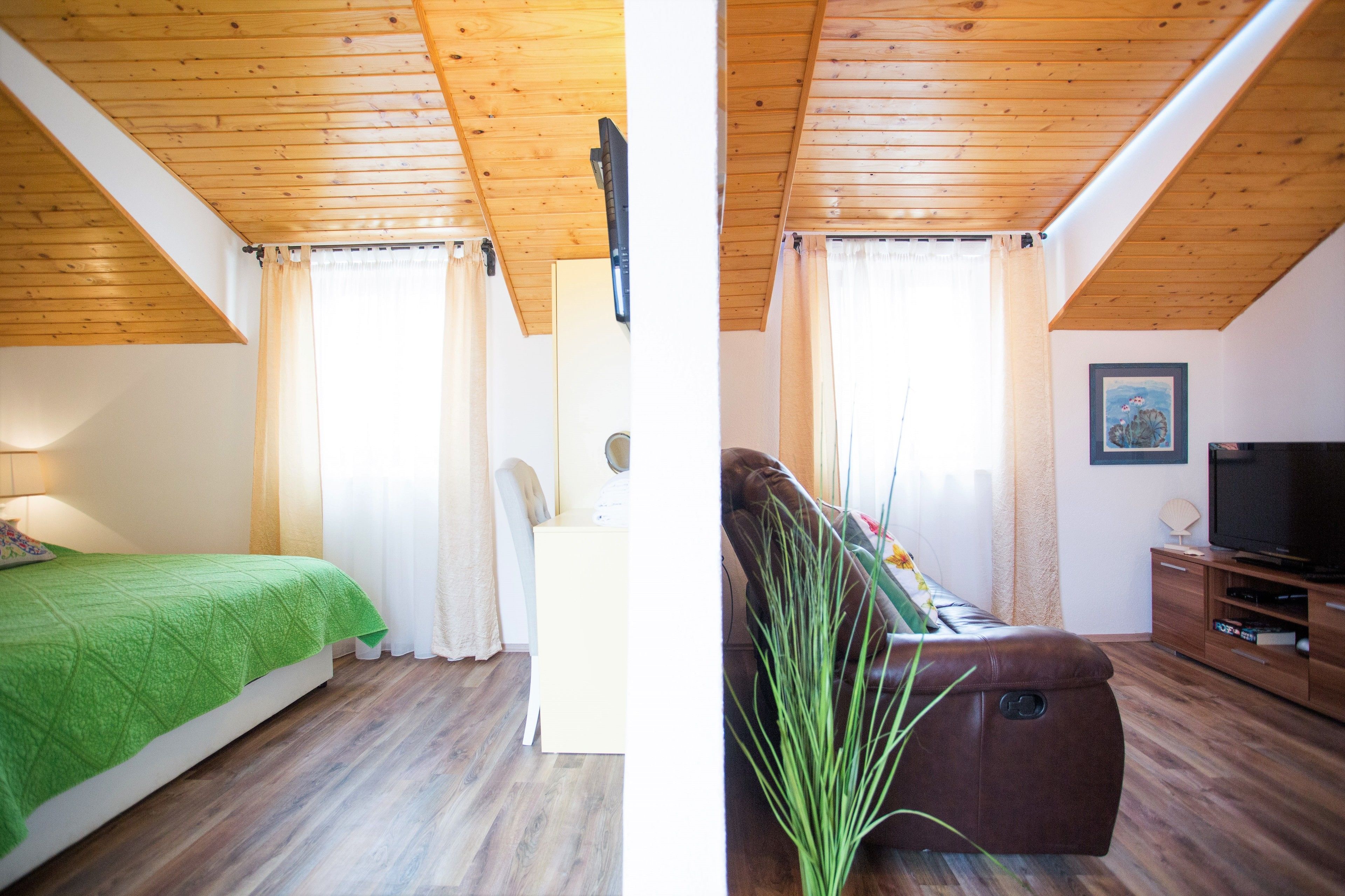 Ein Zimmer mit einem Bett, einem Sofa, einem Fernseher und einer Holzbalkendecke.
