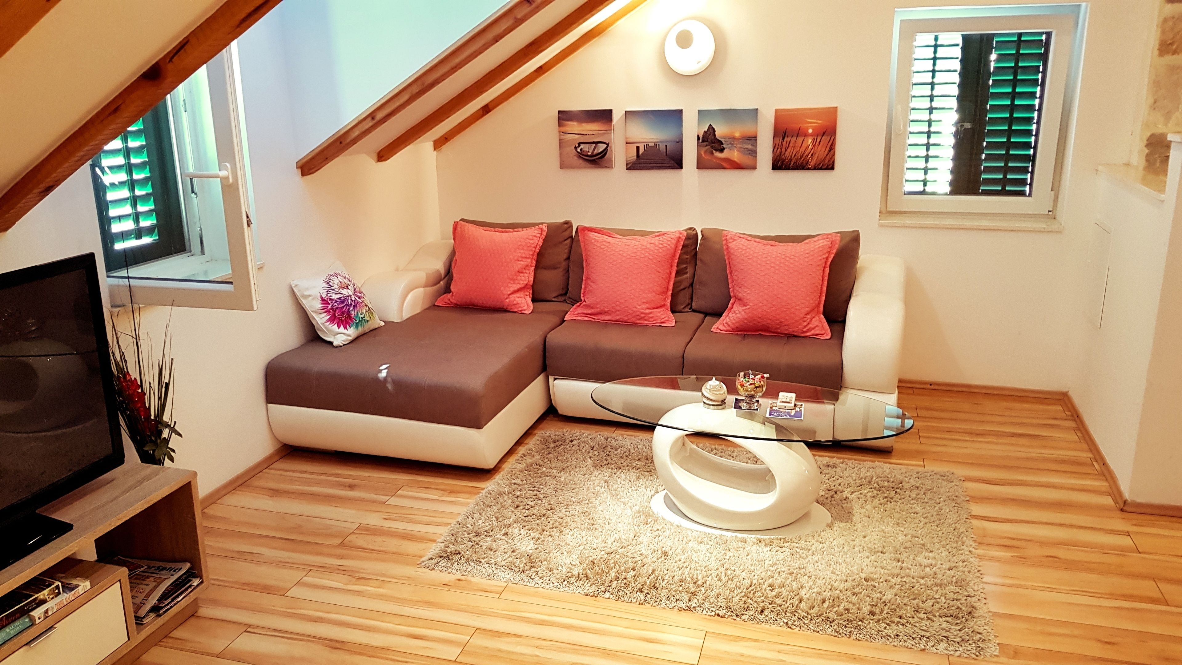 A cozy living room with a sectional sofa, a glass coffee table, and a TV stand.