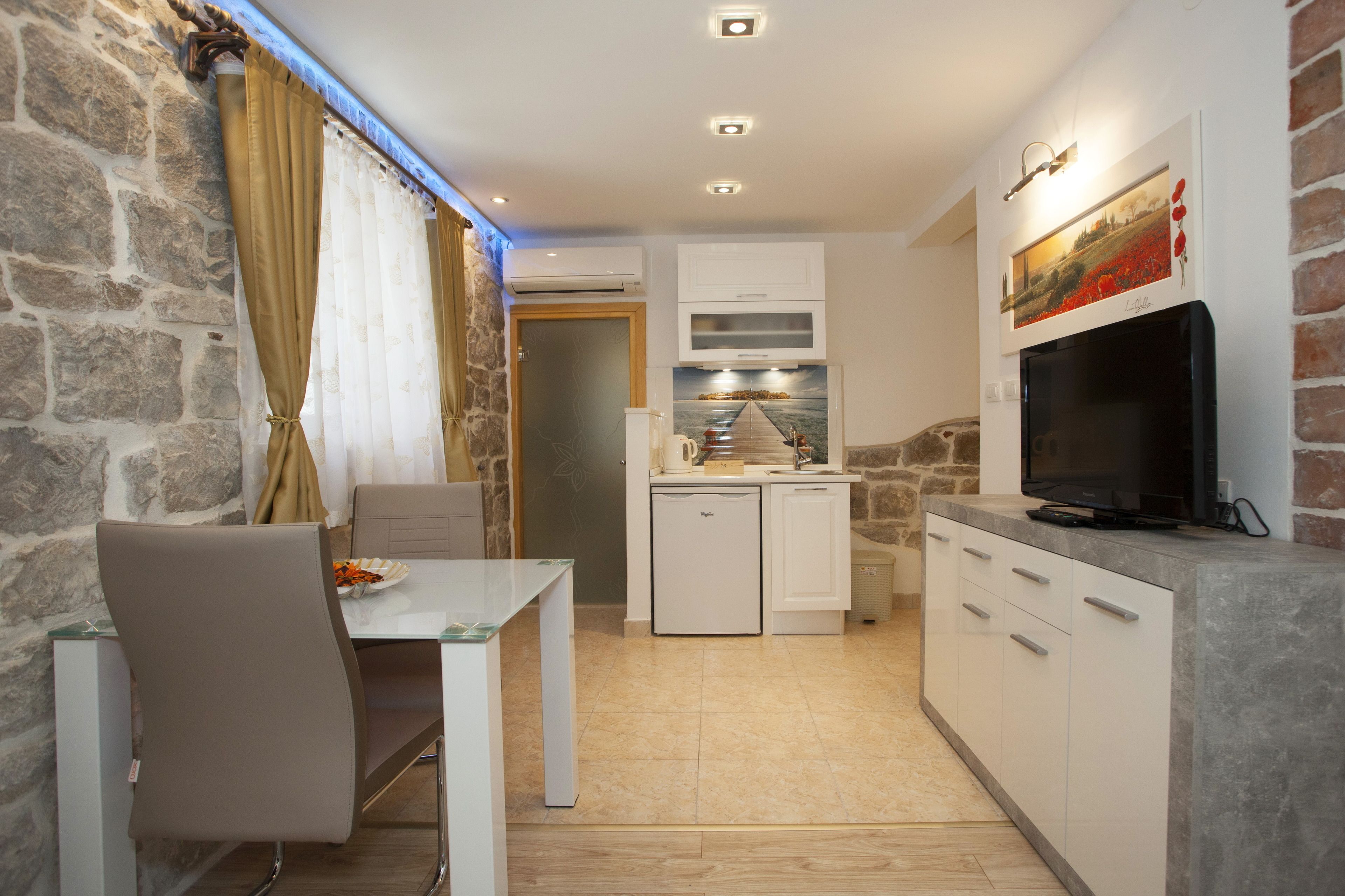A compact kitchen with white cabinets, a built-in oven, and a flat-screen TV mounted on the wall.